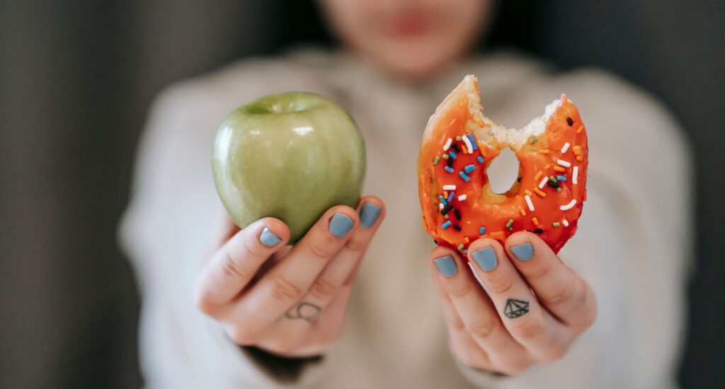 Woman choosing donut over the healthy option of eating an apple
